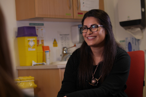 Medical practitioner, wearing a stethoscope in a clinical setting, smiling at the camera 